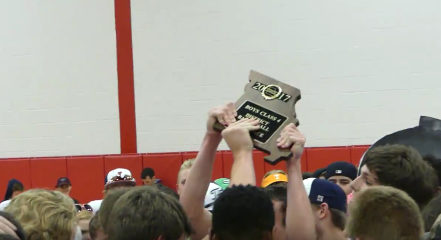 The team holds the plaque proudly in the air, while the student section swarms around them in celebration. 