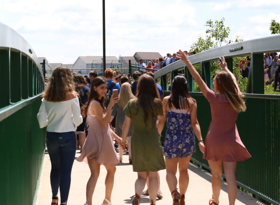 Senior friends hold hands and walk across the bridge for the final time.