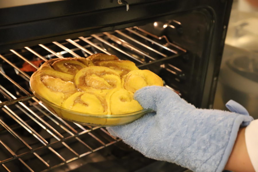Student takes out pumpkin rolls from the oven.