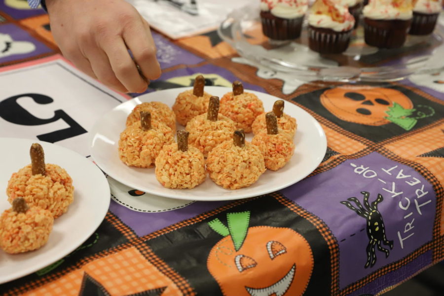 Judge taking a pumpkin rice krispie treat from the creative table of dishes. 
