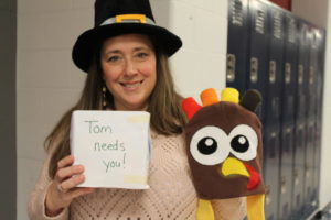 Mrs. T.O. stands in the hallway wearing her pilgrim hat asking for change for the turkey drive.