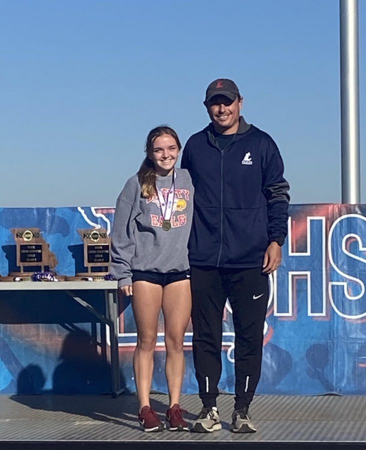 Ally Kruger receives her state champion medal following her course record race at the state meet in Columbia. Coach Glavin stands by Kreger. 
