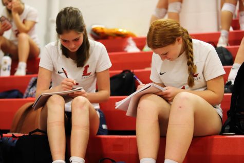 Kinley Jacobi and Victoria Grana do homework in the stands while watching varsitys game against Fort Zumwalt East on Sept. 20.