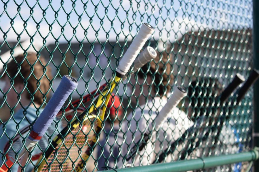 Tennis rackets line the fence as the boys tennis players listen to Coach Campos.