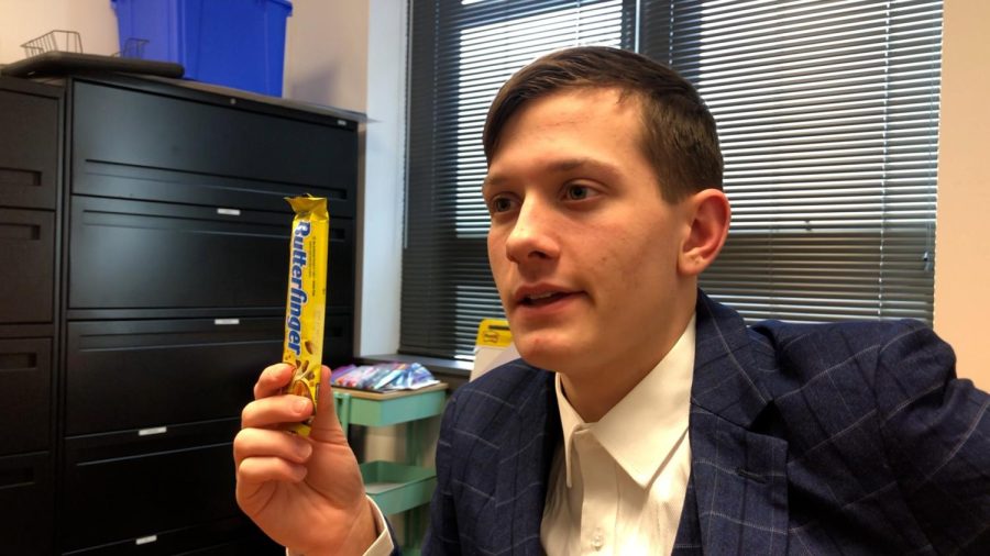 Jax Drezek, playing the Bank Manager, holding up a Butterfinger, a clearly valuable piece.