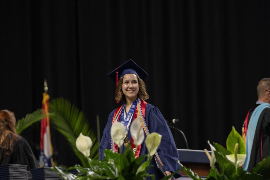 Morgan Feinstein walks across the stage after accepting her diploma while smiling at her friends and family in the audience.