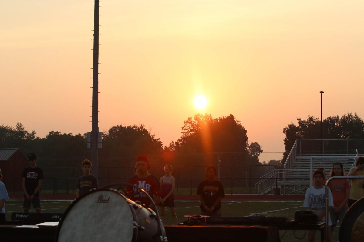 The sun comes up while marching band is practicing in the early morning. 