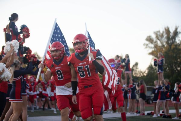 Captain Noah Kuehner and defensive end Aiden King bring out the American Flag and lead the team onto the field before the Red-Out homecoming game against Roosevelt.
