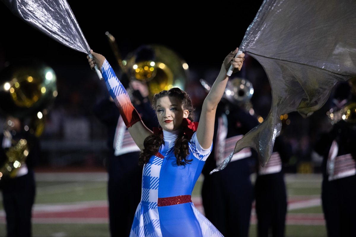 Senior Gracyn Burke twirls two silver flags around during colorguards halftime performance. 