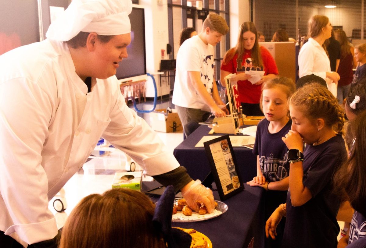 Senior Jacob Kiem offers elementary students an eclair at the showcase event.  
