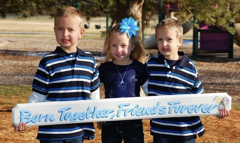 Triplets, Tyler, Amber, and Parker hold up a sign and smile for the camera. (submitted by Amber Sethaler)