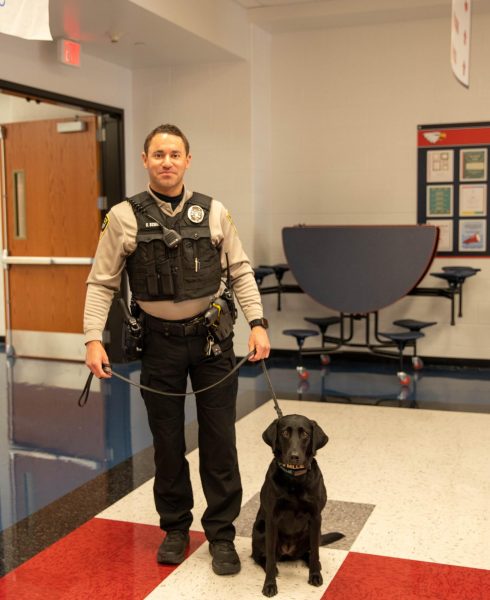 Officer Stephen Schue holding the leash attached to Millie the black lab.