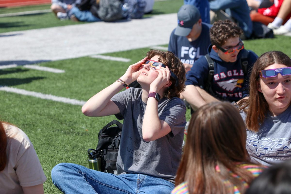 Junior Rachel Church sits on the field with friends as they hold up solar eclipse glasses handed out by the school. These glasses are necessary for to safely view the eclipse. 
