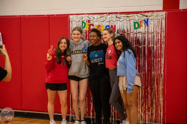 Seniors Kelsey Lynch, Ally Schmelz, Lelani Green, Cora Fairbanks, and Emma Thomas pose in front of the decision day backdrop. 