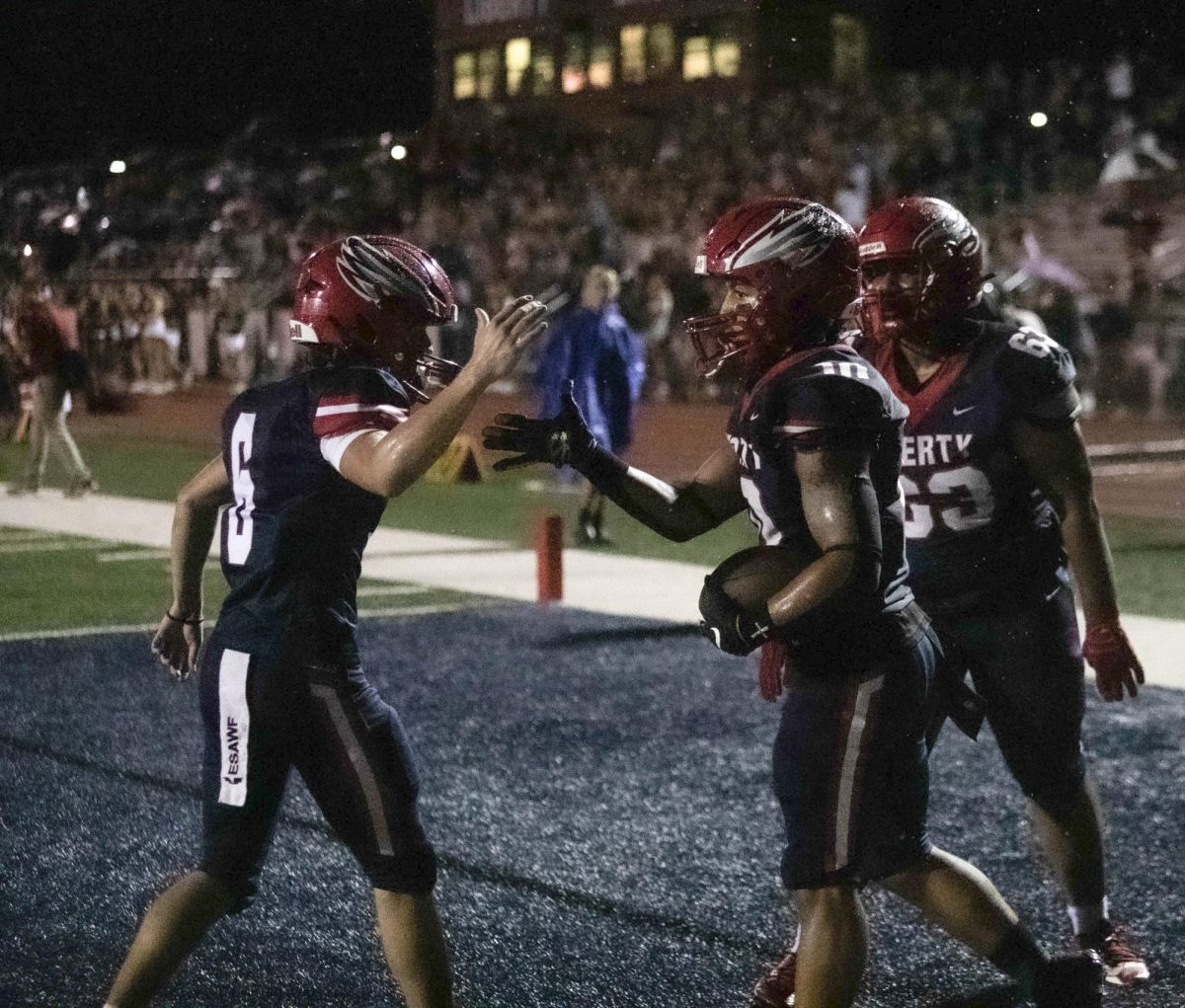 Jaylen Mack (12) high fives teammate Caiden Galati (11) after scoring a touchdown in the rain while teammate CJ McClain (10) joins the celebration. 