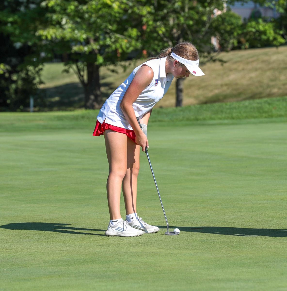 Jenna Means (10) lines up her club tto lightly swing her club to the hole at the golf match against Troy Buchanan on Payton Lindsay (9) lines up her club to the ball on the rough during the golf match against Troy Buchanan on Sept. 5.