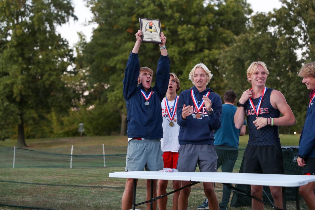 Landon Jones (12) holds up the varsity boys GAC Conference Champions plaque while celebrating at McNair Park.