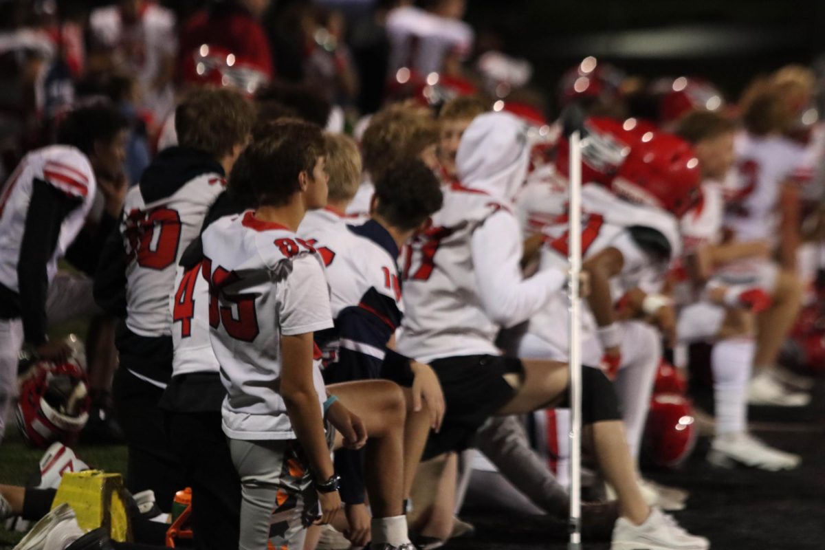 The varsity football team kneels in respect as an injured player receives medical attention on the field.