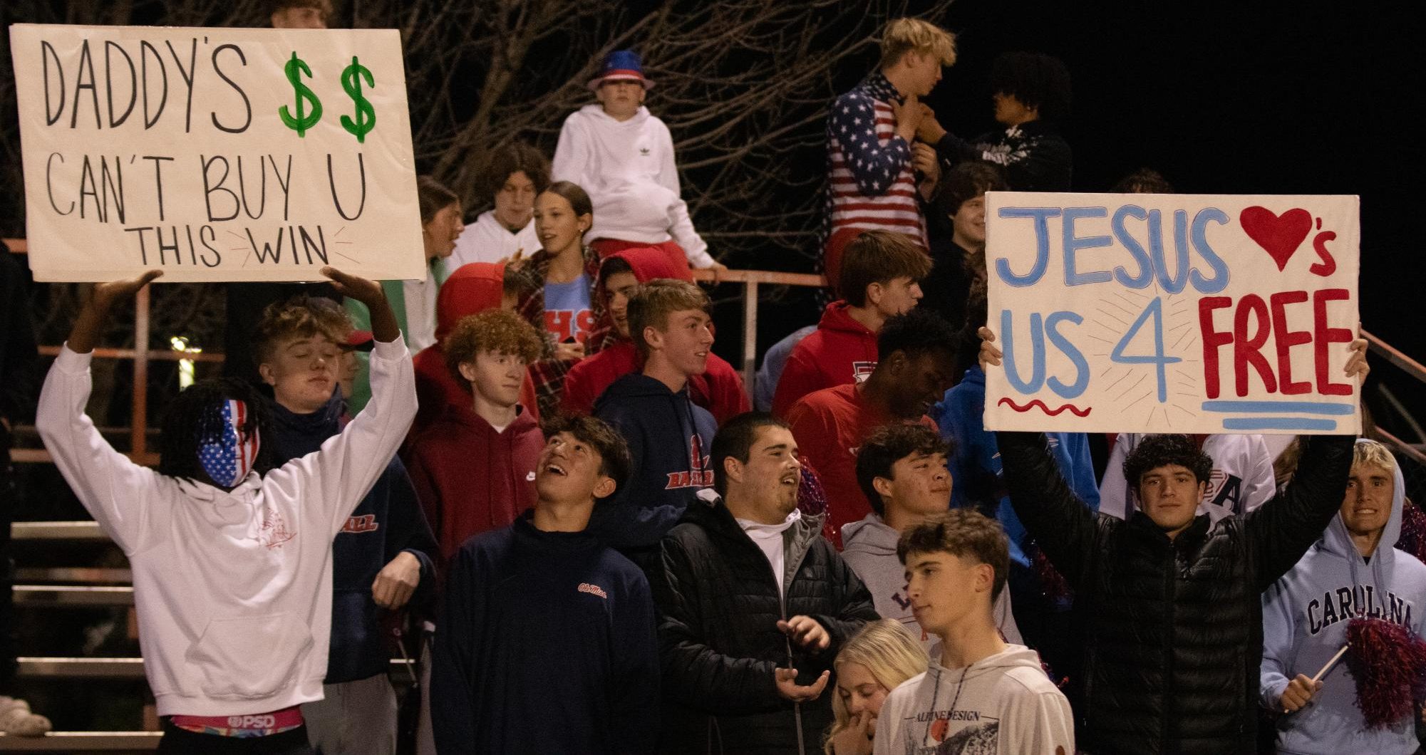 Terran Smith (12) and Jack Ryan (12) hold up signs in the student section at the soccer district championships.