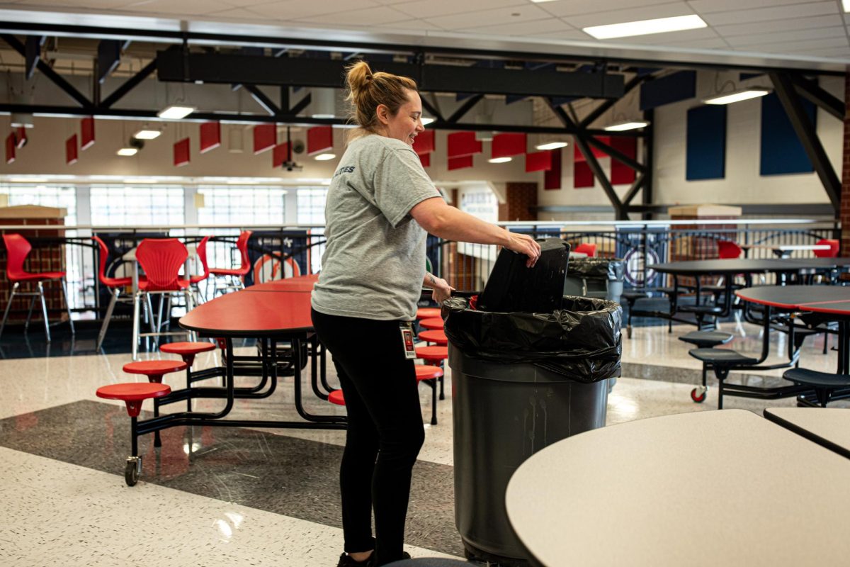 Jacquelyn Hamby empties out her dustpan after sweeping around cafeteria tables.