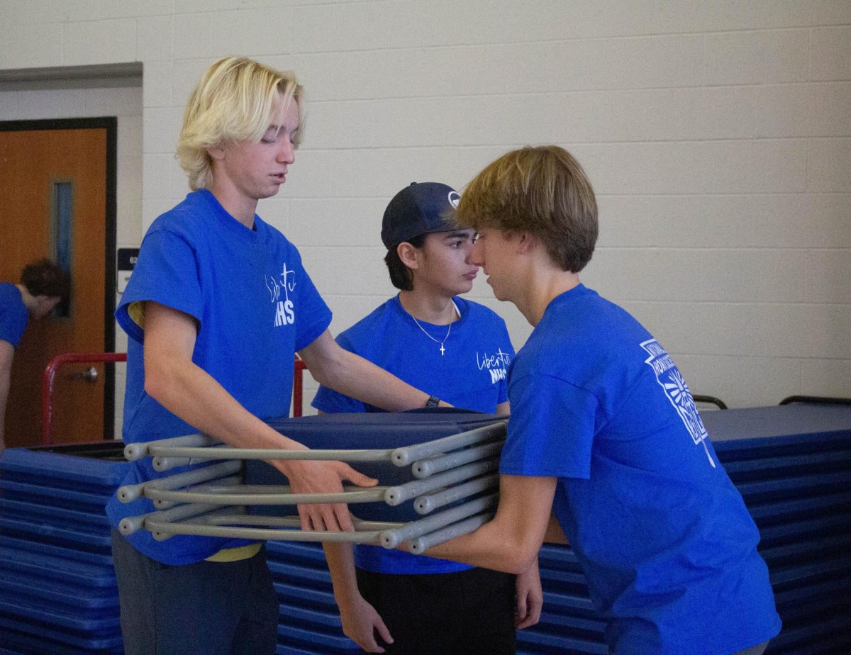 NHS students Nate Wietbrock (11) and Ethan Coleman (11) work together to stack up the foldable chairs in the lunchroom. 