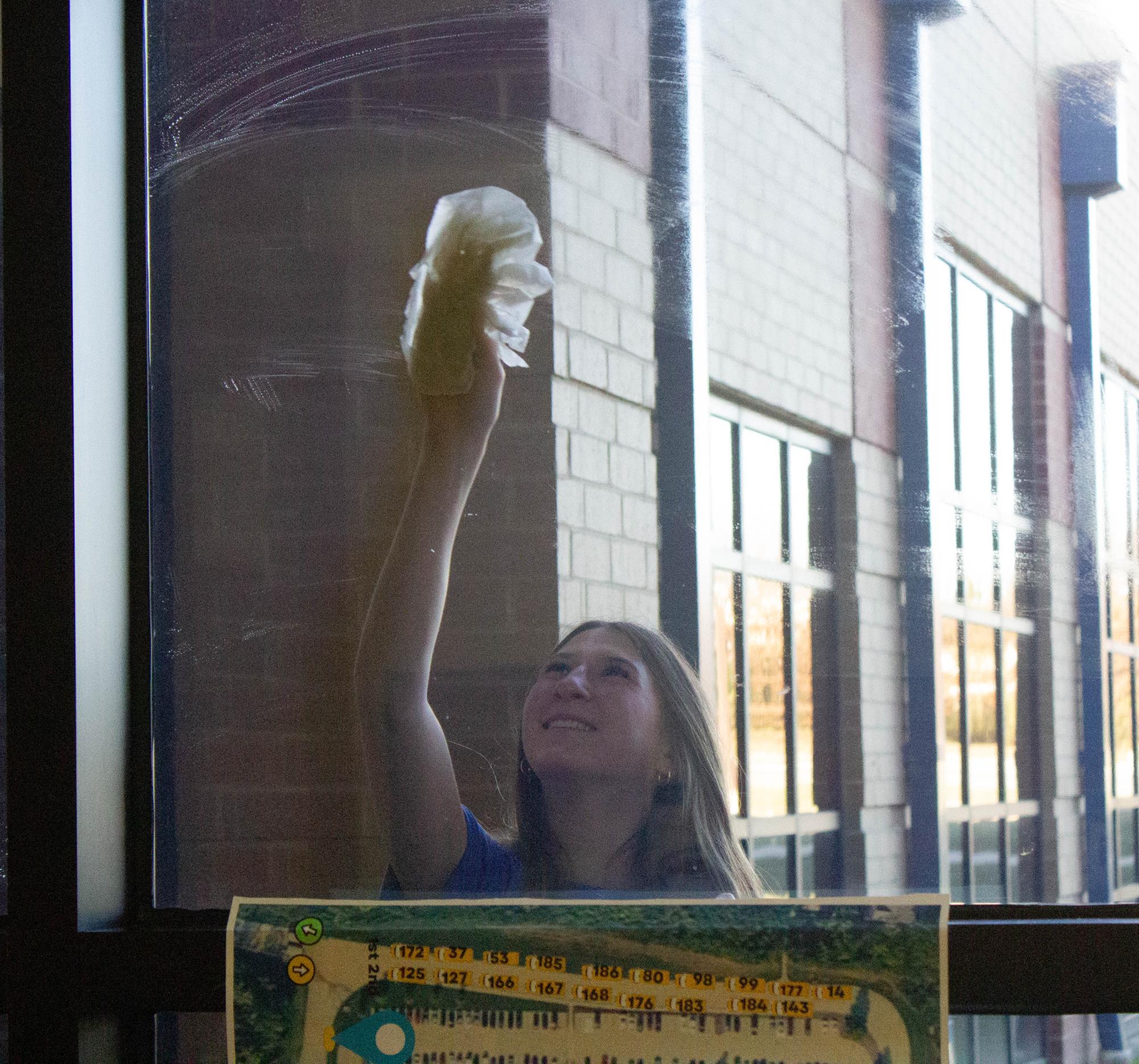 NHS student Olivia Fehling (11) steps outside to clean the window to the side entrance door.  