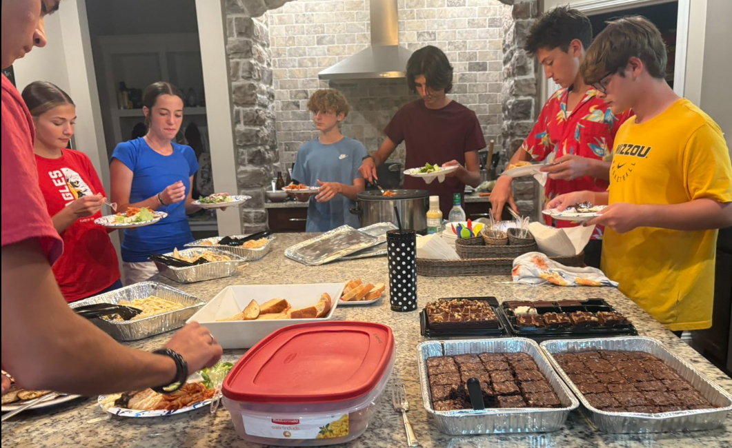 The cross country team serves themselves pasta and other foods.