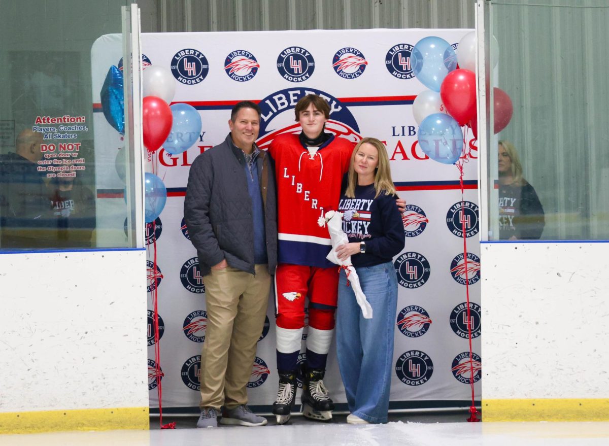 Max Westhoff (12) poses with his mom and dad in front of Liberty Hockey backdrop for senior night.