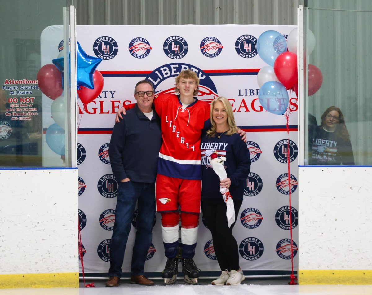 Jude Bill (12) poses with his mom and dad in front of Liberty Hockey backdrop for senior night.