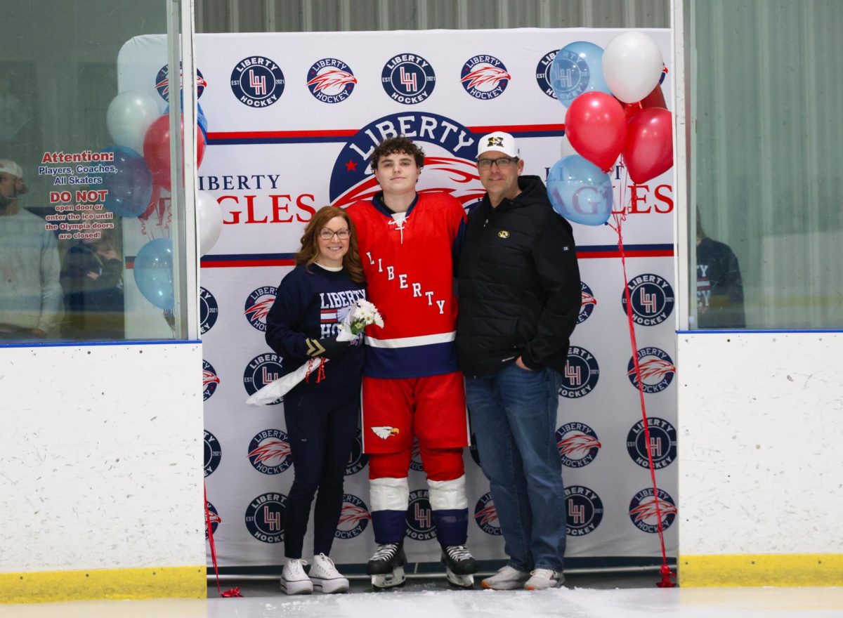 Carson Brassel (12) poses with his mom and dad in front of Liberty Hockey backdrop for senior night.