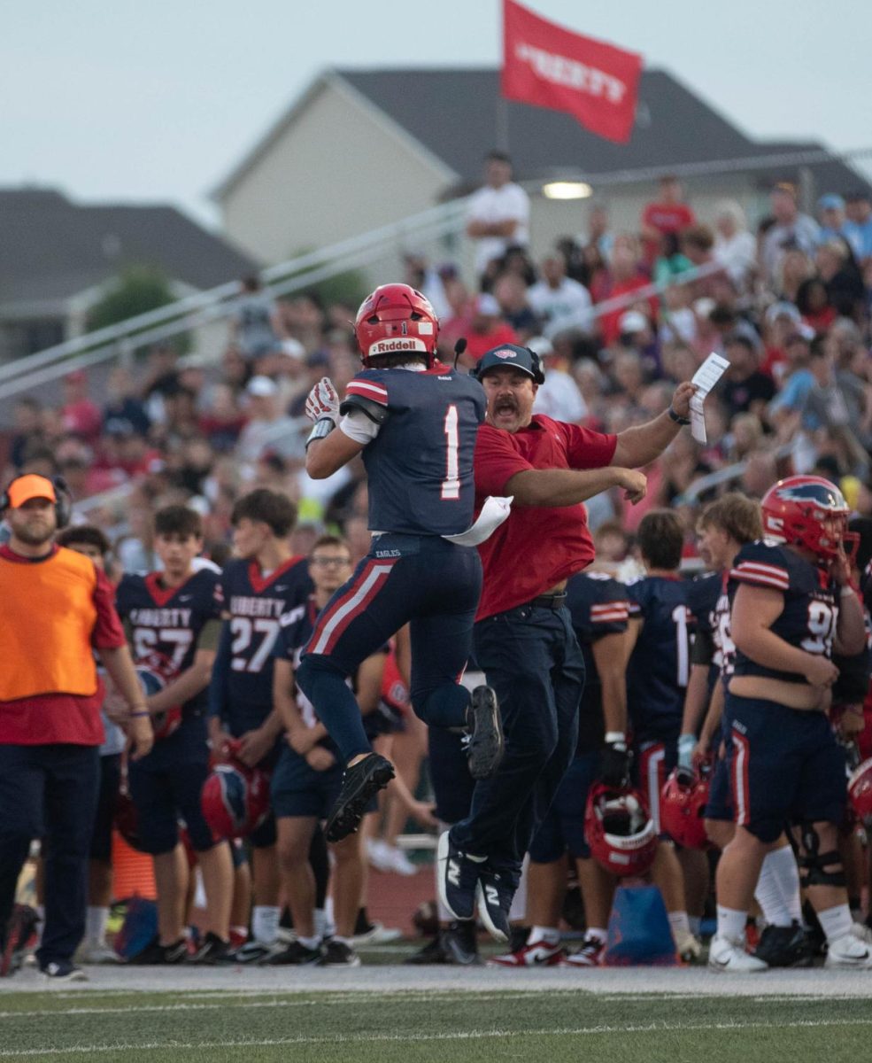 Coach McMillen bumps shoulders with Caleb Orcutt (11) during a game against Warrenton. In addition to football in the fall, McMillen is now coaching the girls flag football team this spring. 