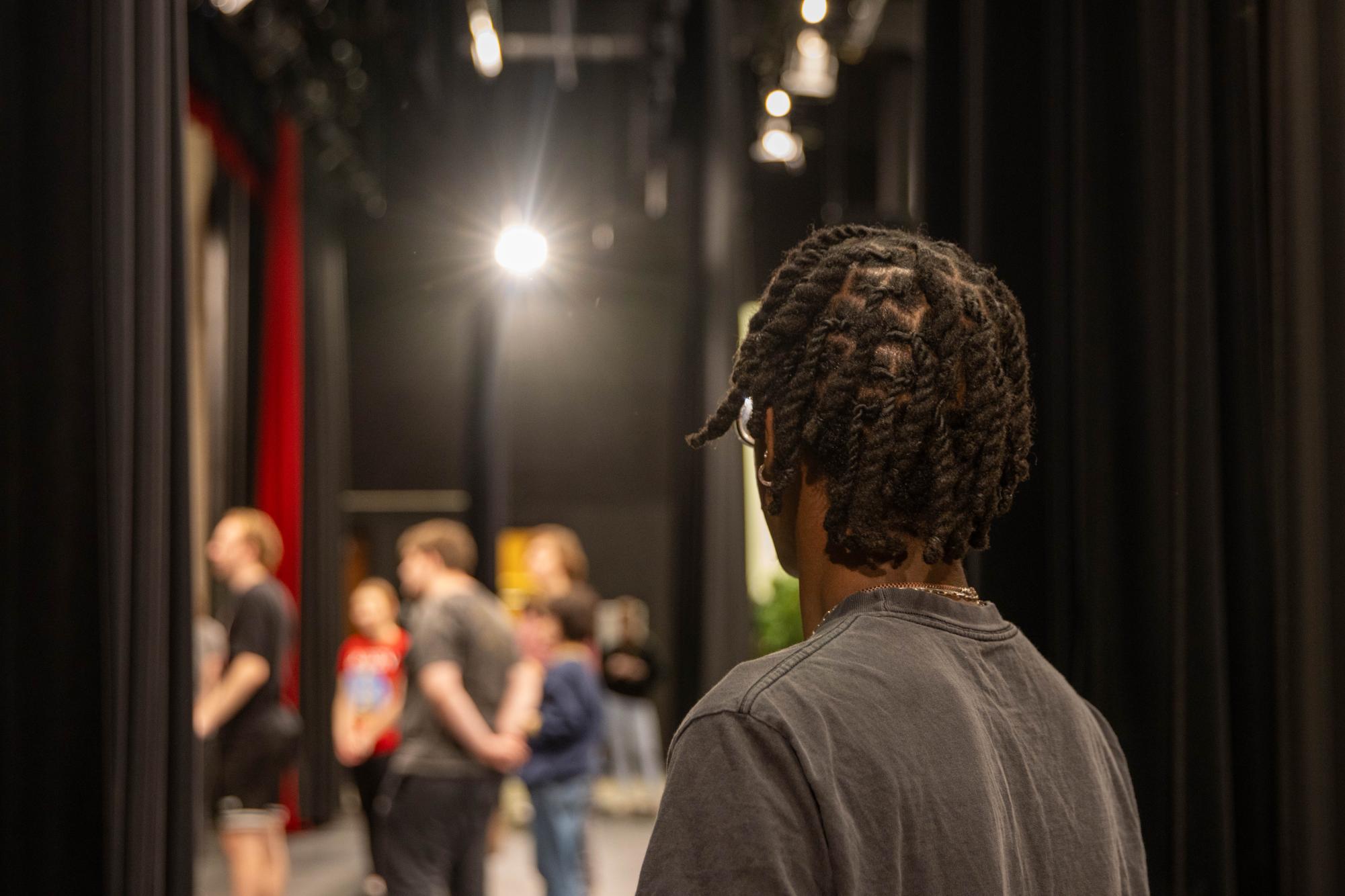 Marquise Buckley stands in the wings of the theater as his fellow castmates rehearse choreography for the number, “The Farmer and the Cowman.”