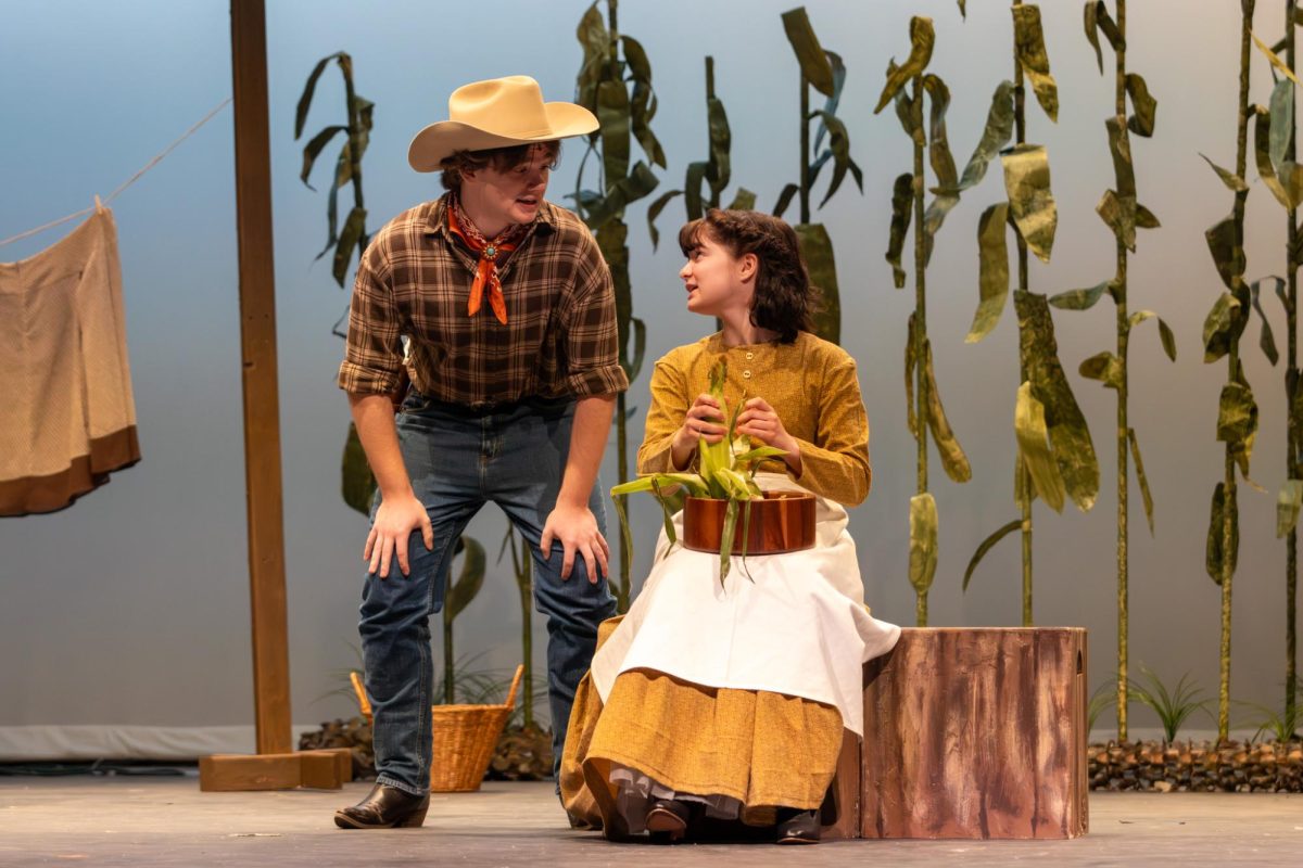 Curly, played by Tyler Bugg (12), talks with Aunt Eller, played by Micki Morris (12), as she shucks corn. The stage directors decided on purchasing real corn for the scene, rather than constructing prop corn.