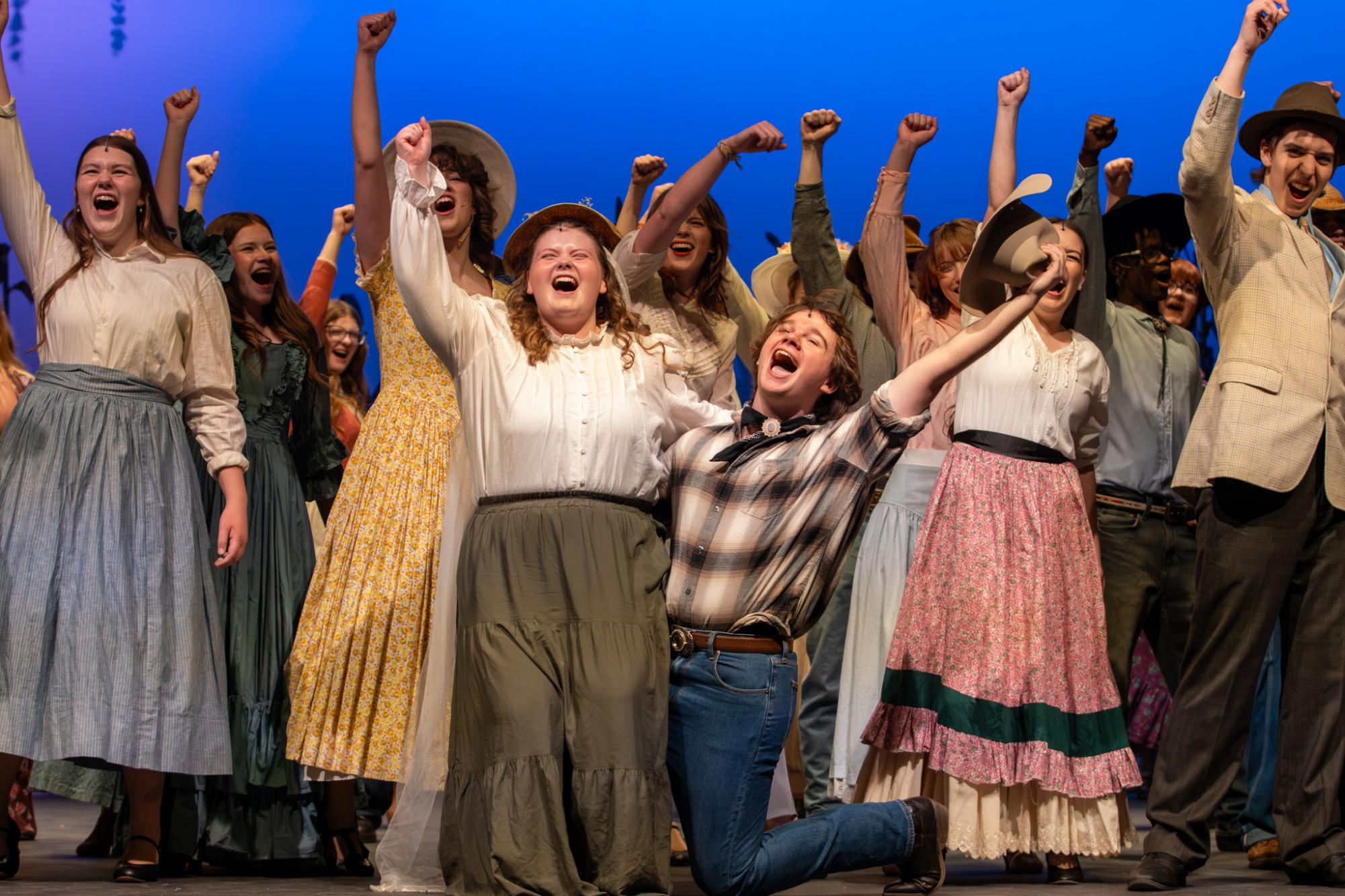 The cast pump their fists in celebration, as the title song, "Oklahoma" concludes. This song requires the most amount of practice from cast members, as it featured a four-part harmony.