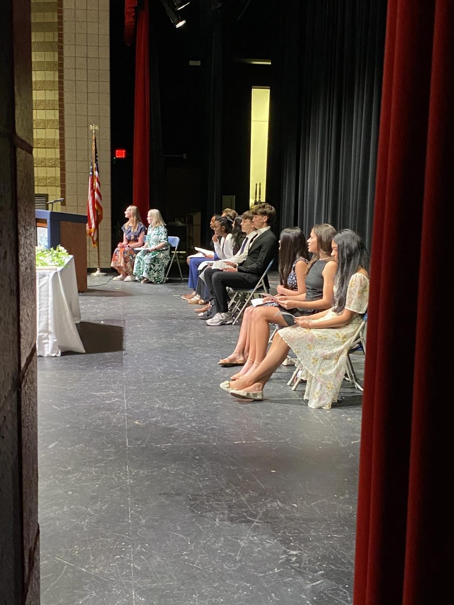 The NHS sponsors, retiring officer team, and incoming officer team sit together on stage as Inductions take place. 